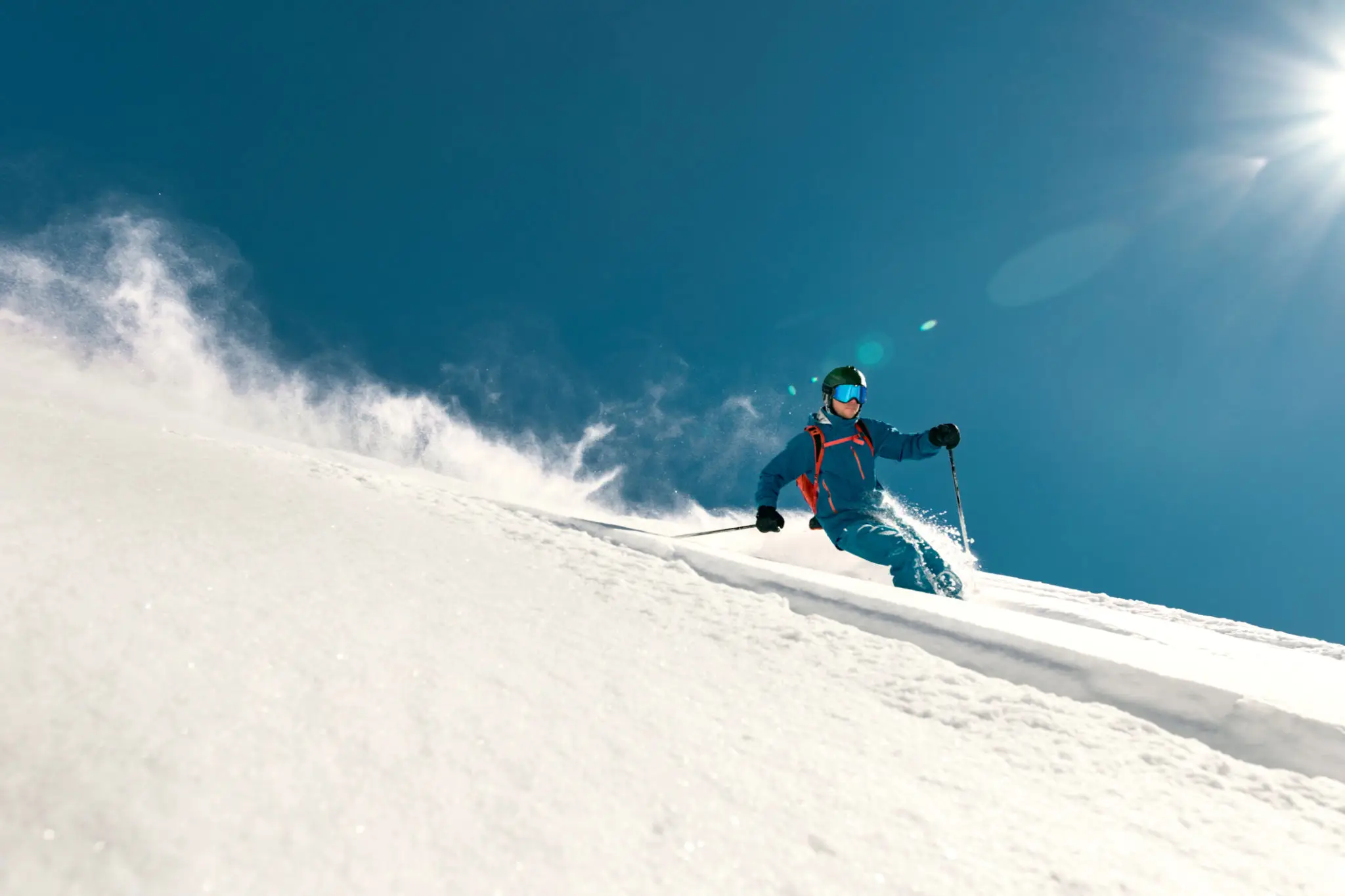 Skier carving down snowy slope under blue sky